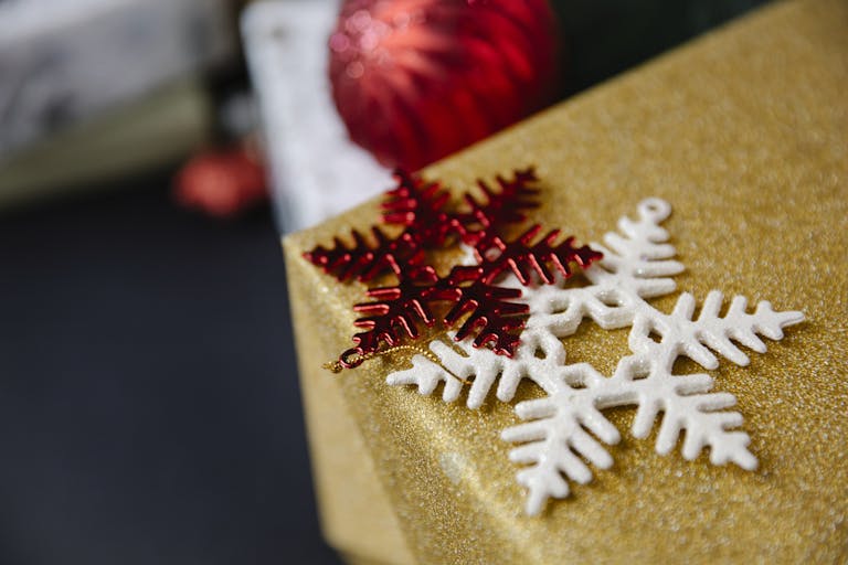 Close-up of a golden gift box adorned with snowflake ornaments and a red bauble, capturing the festive spirit.